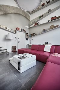 Salón de tonos blancos donde se puede ver un sofá y diferentes estanterías desestructuradas. 